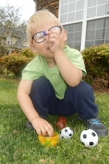 young boy sitting on the grass smiling looking at little sport balls young boy sitting on the grass smiling looking at little sport balls